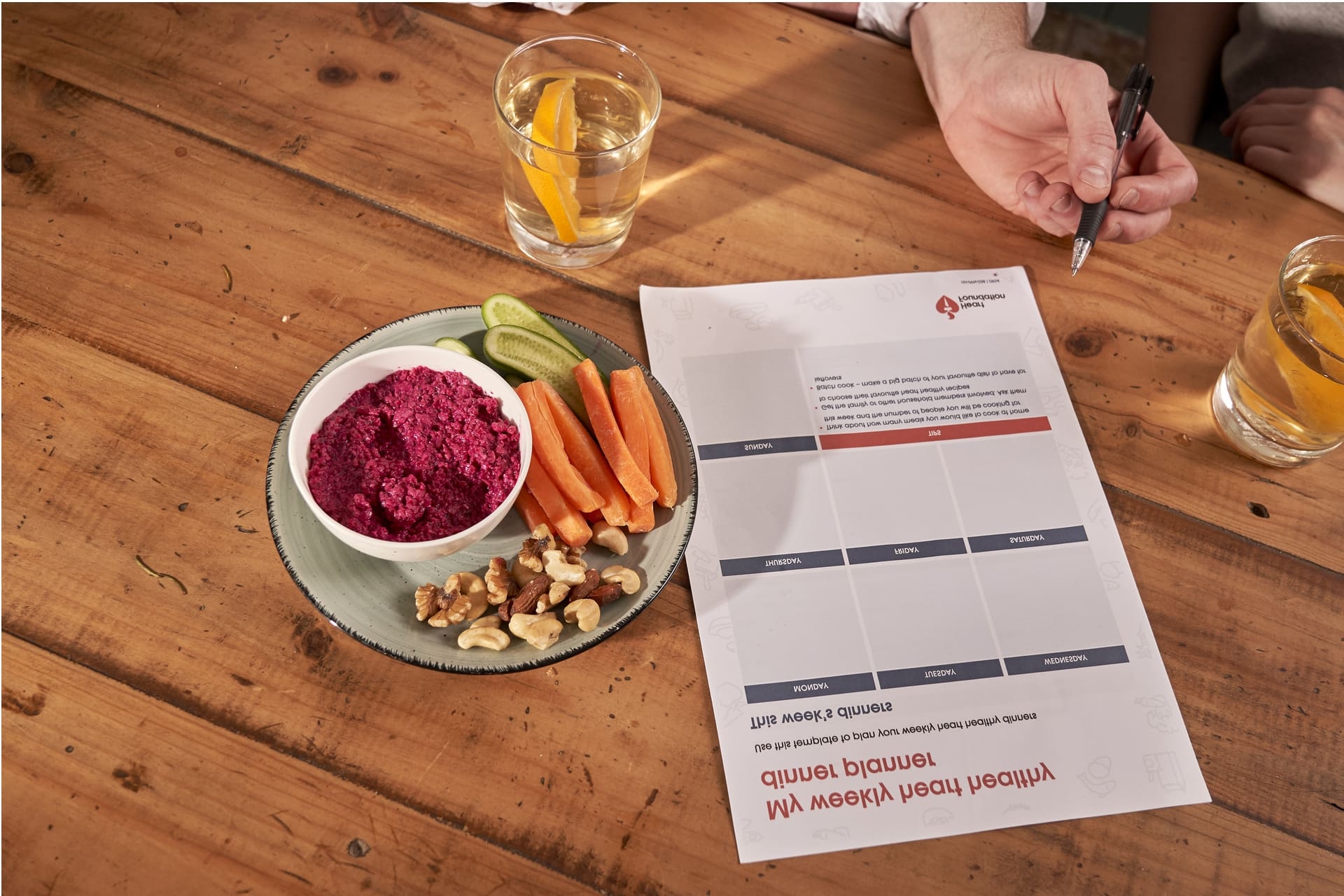 Resources for heart-healthy meal plans on a table beside a glass of water and healthy snacks