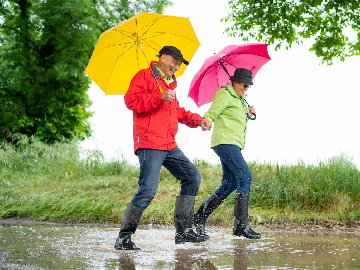 Happy senior couple in black rubber boots taking a walk on rainy day.