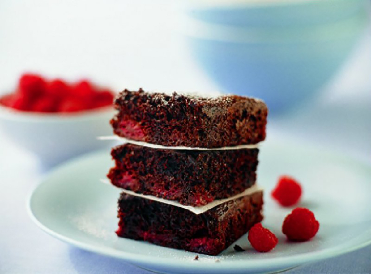 Three chocolate brownies topped with fresh raspberries on a white plate