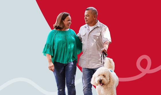 A happy couple walking their fluffy white dog on a background of red and grey
