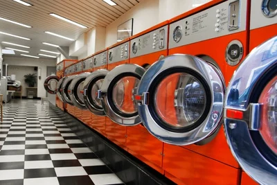 A row of orange washing machines in a laundrymat with the doors open
