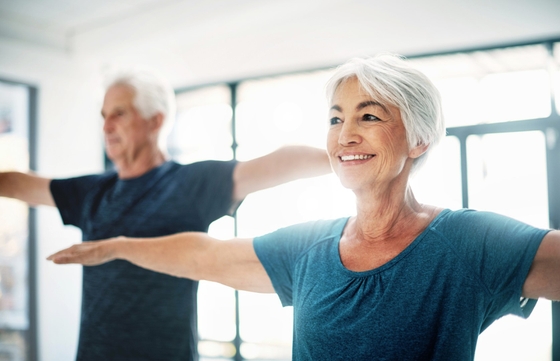 An older couple engaging in stretching exercises in a room, promoting physical fitness and flexibility.