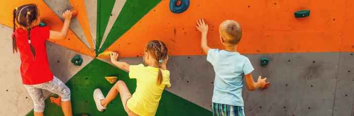 two girls and one boy climbing on a colorful climbing rock