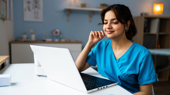 Female doctor in a blue medical scrubs, using laptop at the modern ordination