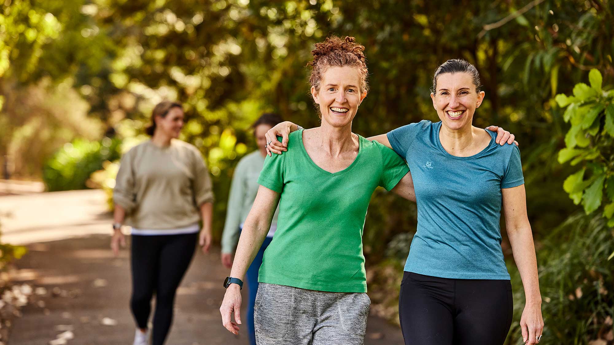 Two women arm in arm smiling as they walk, in their exercise gear