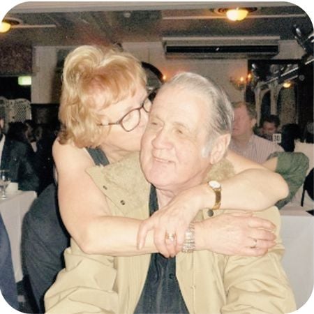 Woman with arms around husband who sitting down at down