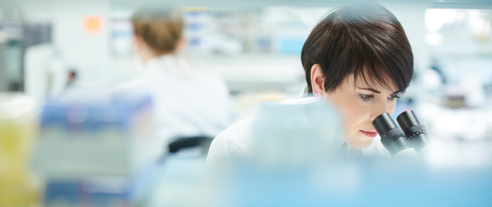 A female scientist in a lab coat examining a specimen under a microscope.