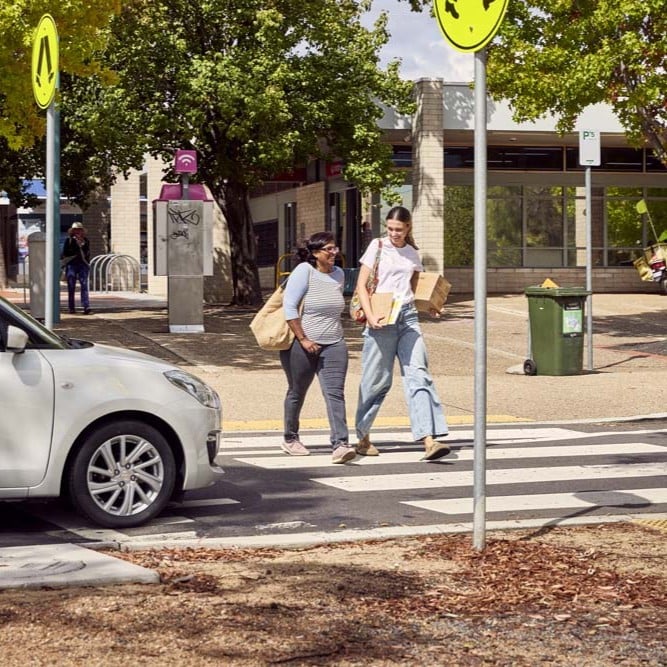 Two people crossing a pedestrian crossing in an urban area.