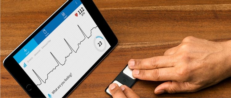 A person measuring their heart rate using their fingers on a device and a monitor tablet