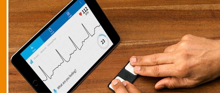 A person measuring their heart rate using their fingers on a device and a monitor tablet