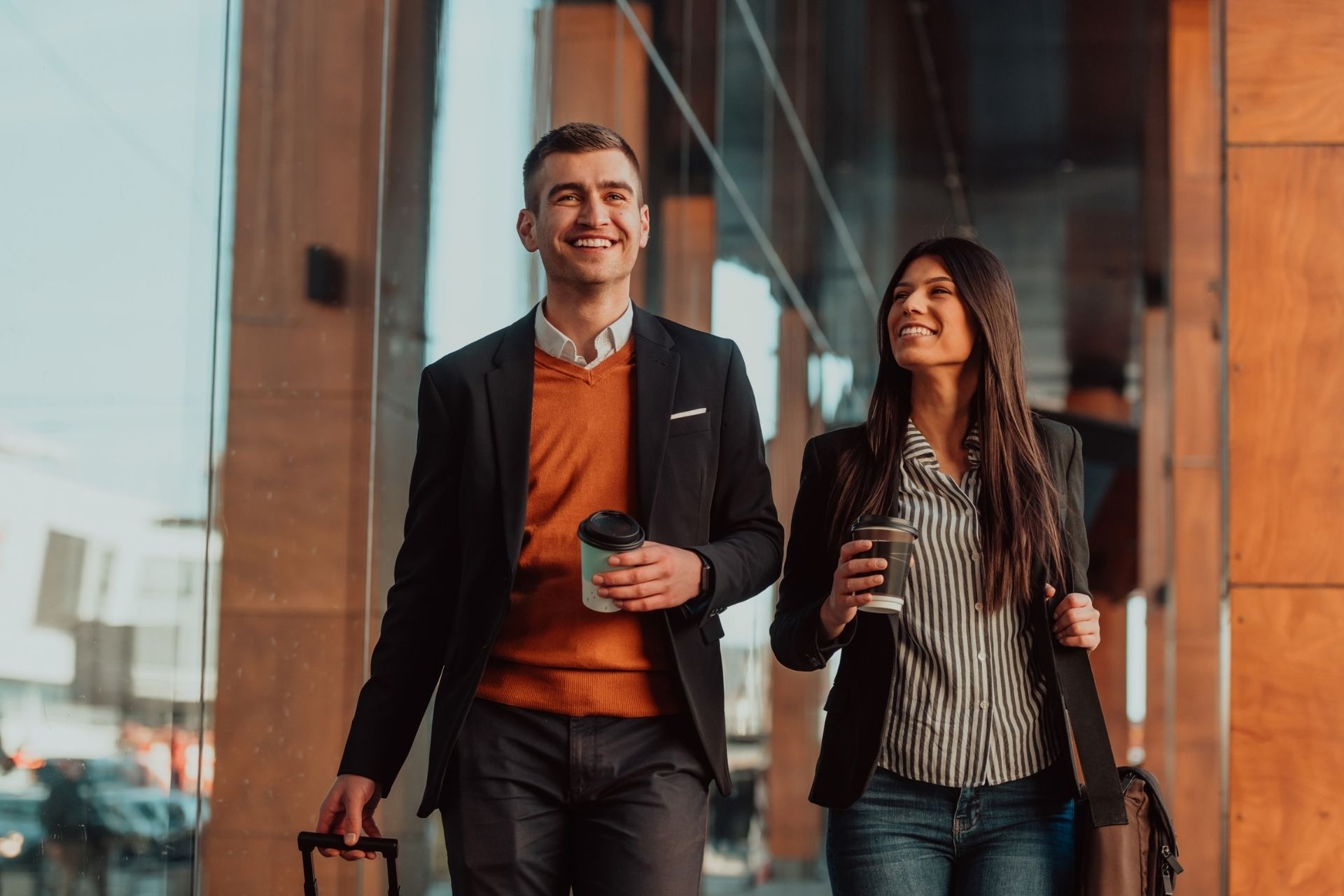 Two travelling researchers talking and holding luggage traveling on a business trip, carrying fresh coffee in their hands.