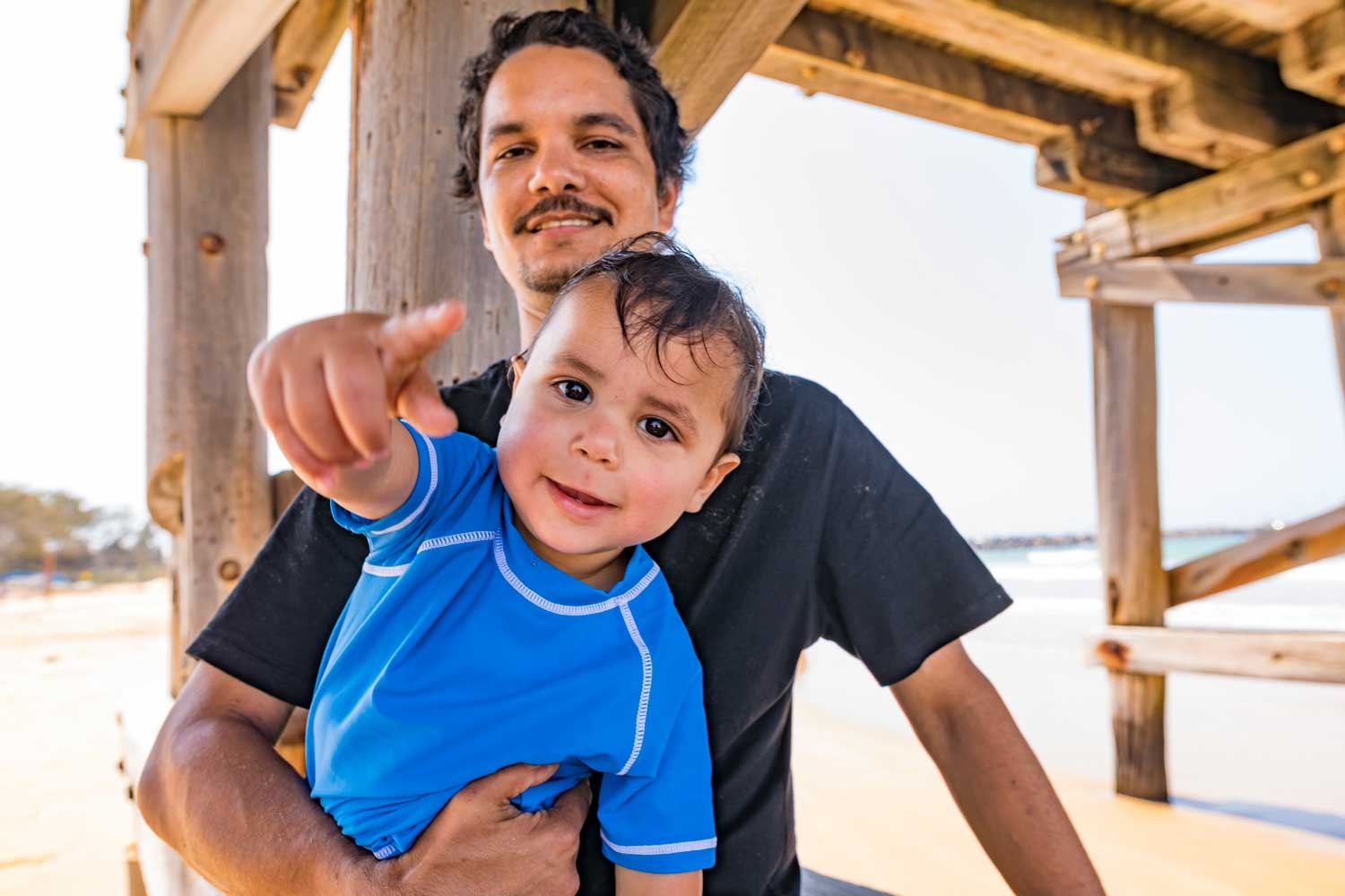 Young Aboriginal man with his son under a jetty at the beach