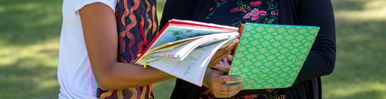 Two women standing with view of their hands holding a notebook