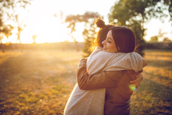 Two women embracing each other warmly in a picturesque field as the sun sets in the background.