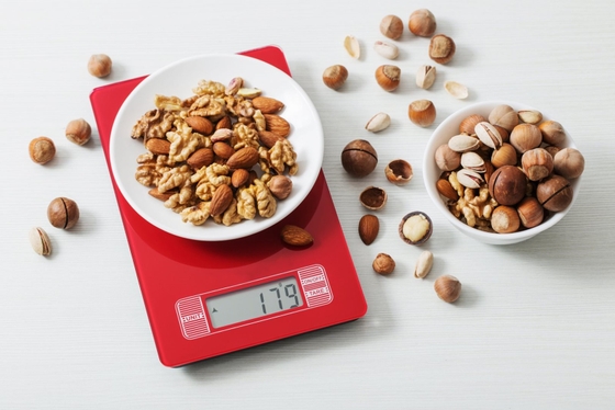 A scale with various nuts placed on it, including almonds, walnuts, and peanuts.