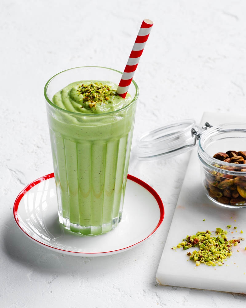 Pouring pistachio smoothie into a tall glass