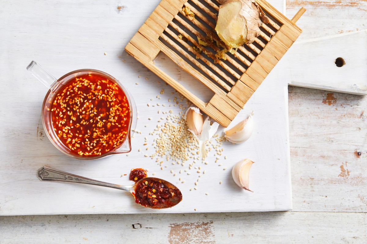 A bowl of chili sauce, a spoon, and a wooden cutting board placed together
