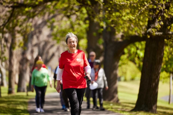 Woman with grey hair, wearing red HF t-shirt, walking and smiling, ahead of other walkers