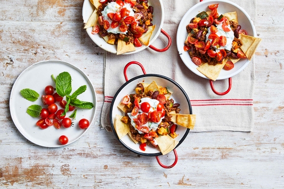 Three bowls of nachos with toppings on a table