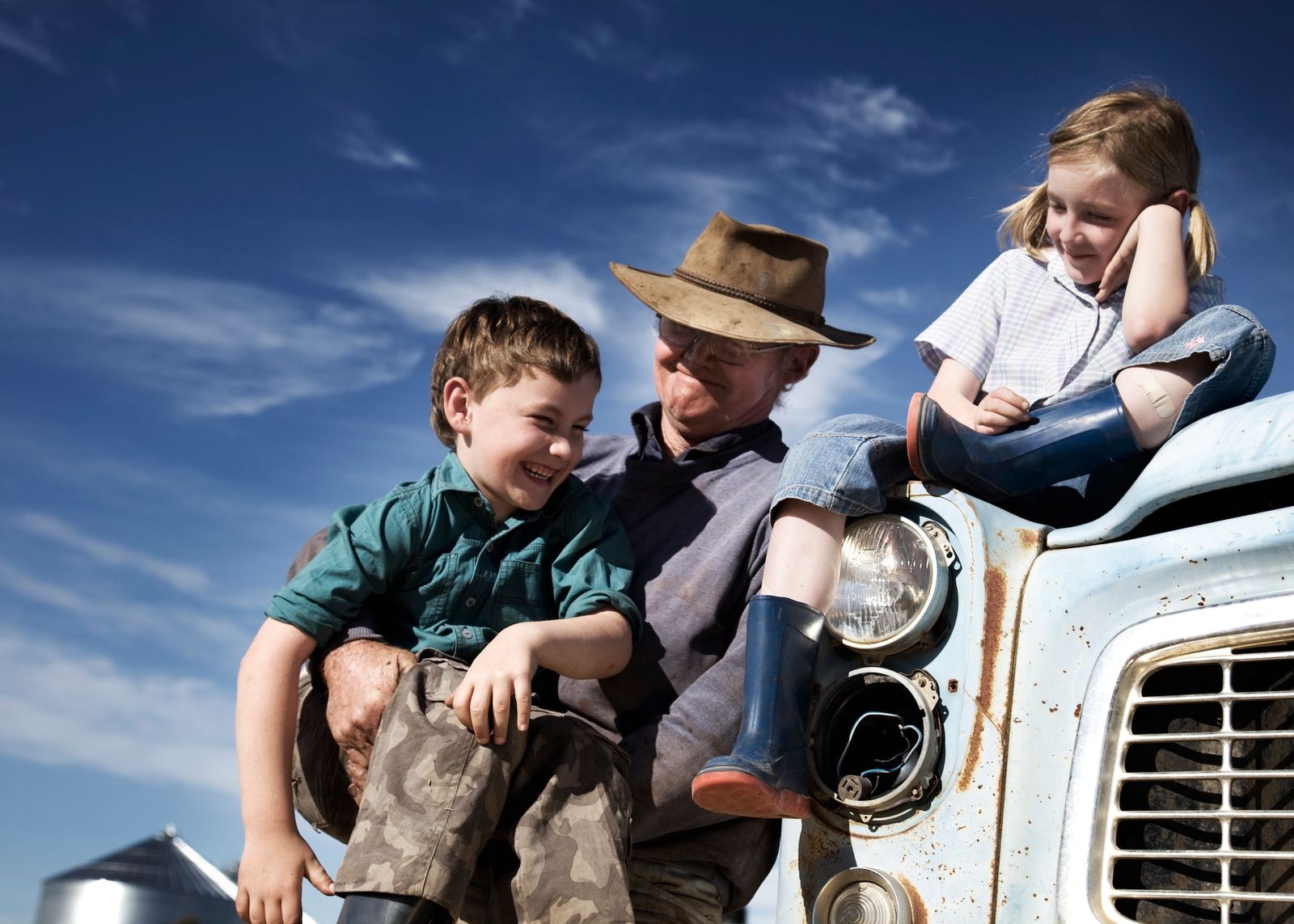 A man and two children sitting on the hood of a truck, enjoying a moment of togetherness.