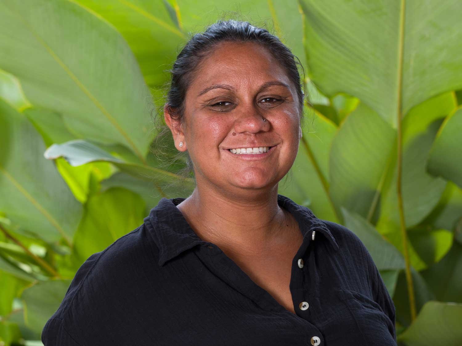 headshot of a women smiling while standing in front of a leafy green background 