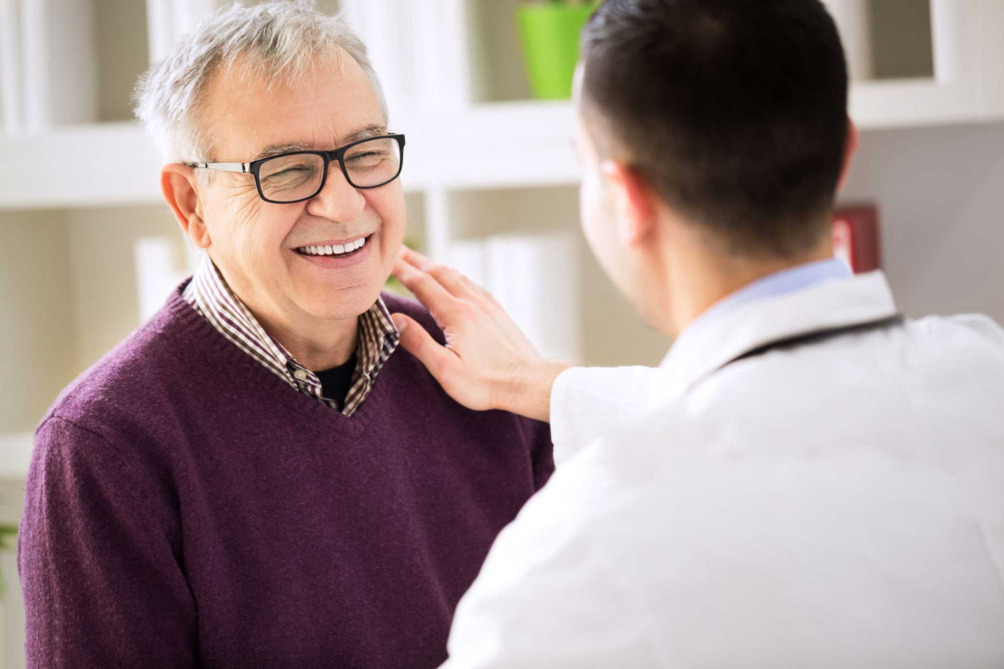 Older male patient smiling with GP, whose hand is on his shoulder