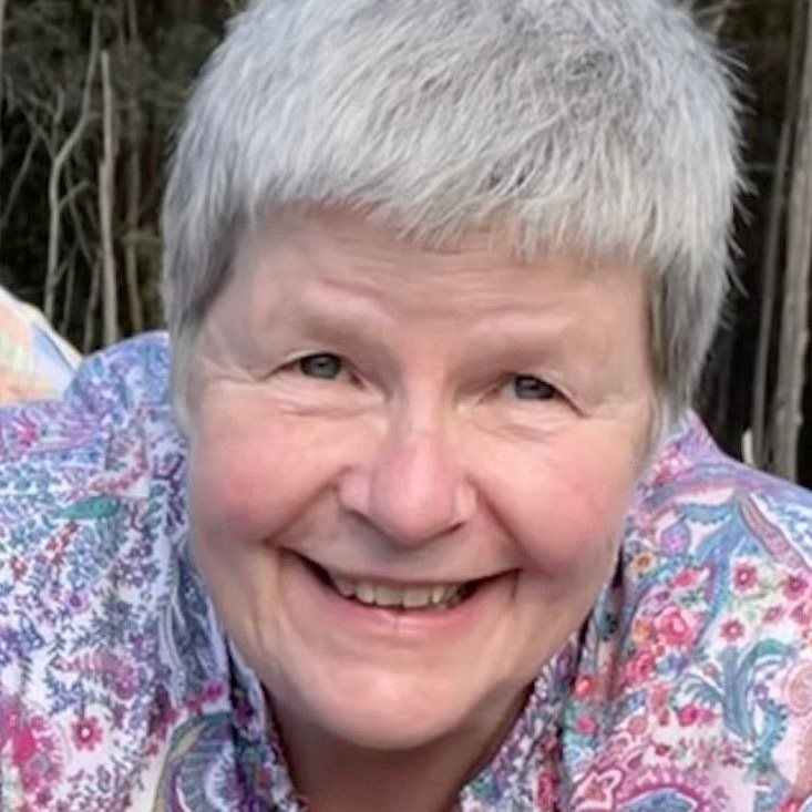 Prof Jan Radford with grey hair smiling warmly for the camera, radiating joy and contentment.