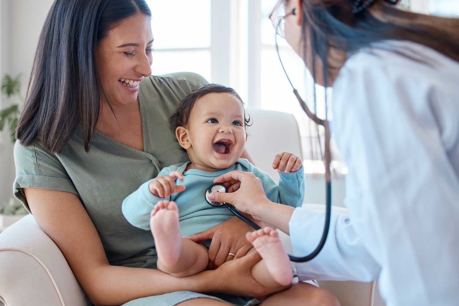 Mother and baby, laughing as doctor holds stethoscope on happy baby's chest