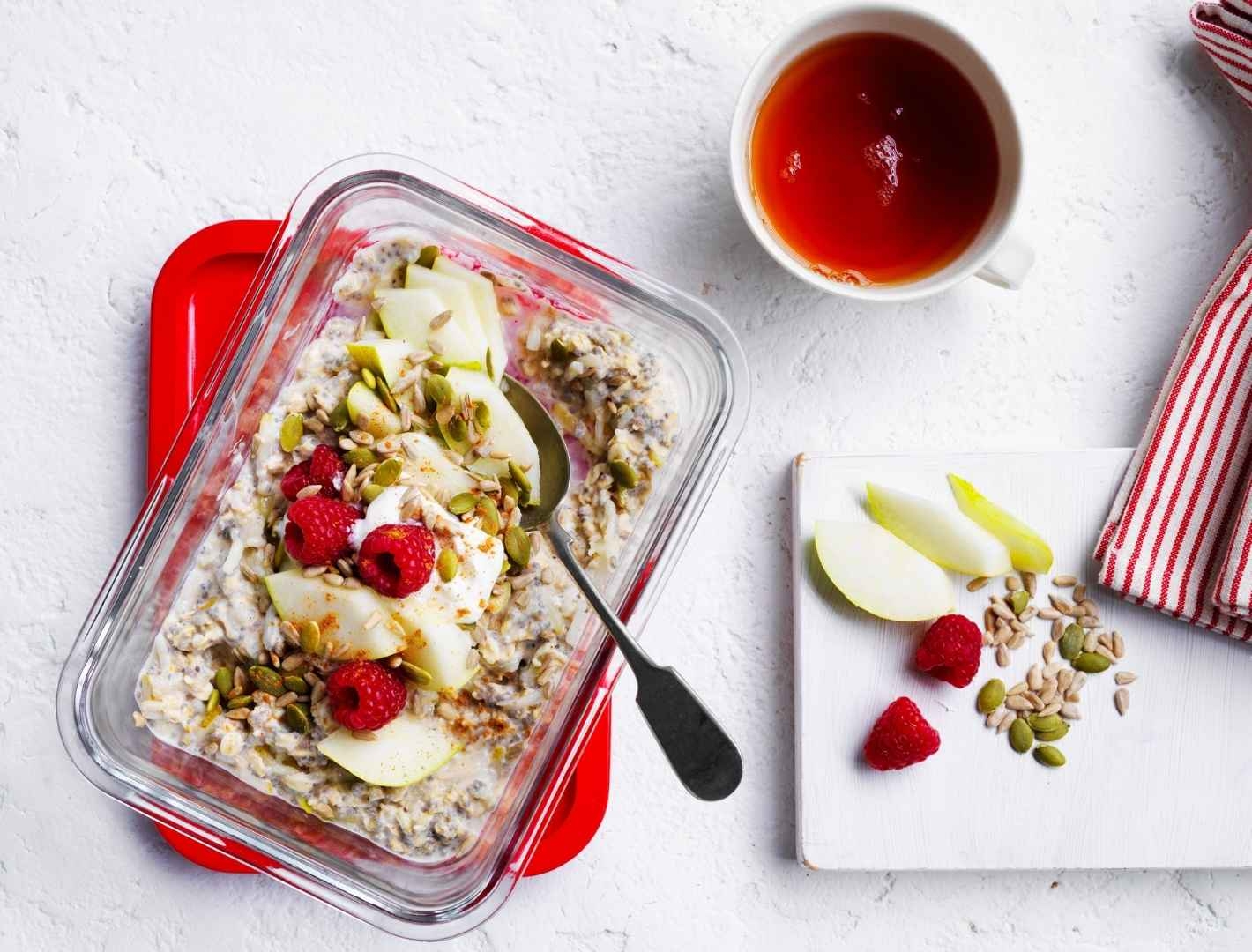 Chai overnight oats in glass baking dish on table with maple syrup and pear