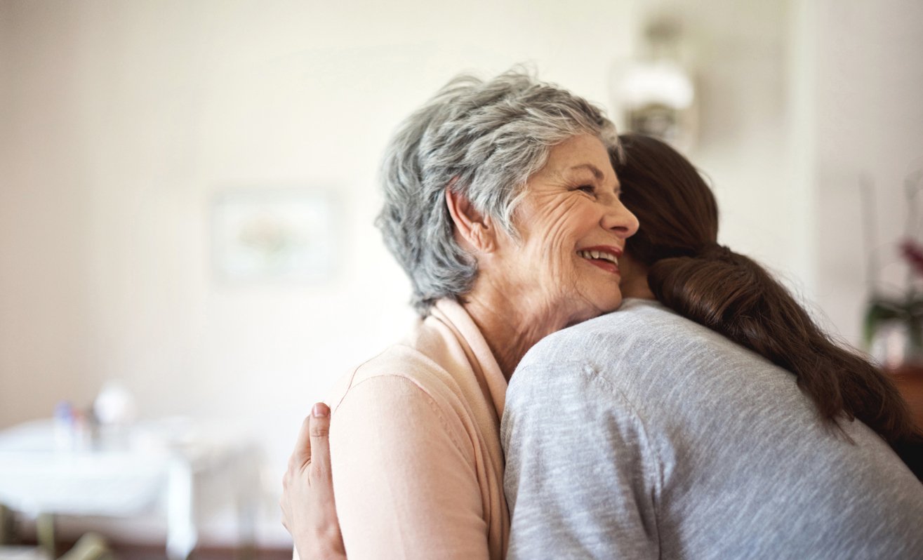A woman embracing an older woman in a cozy living room.