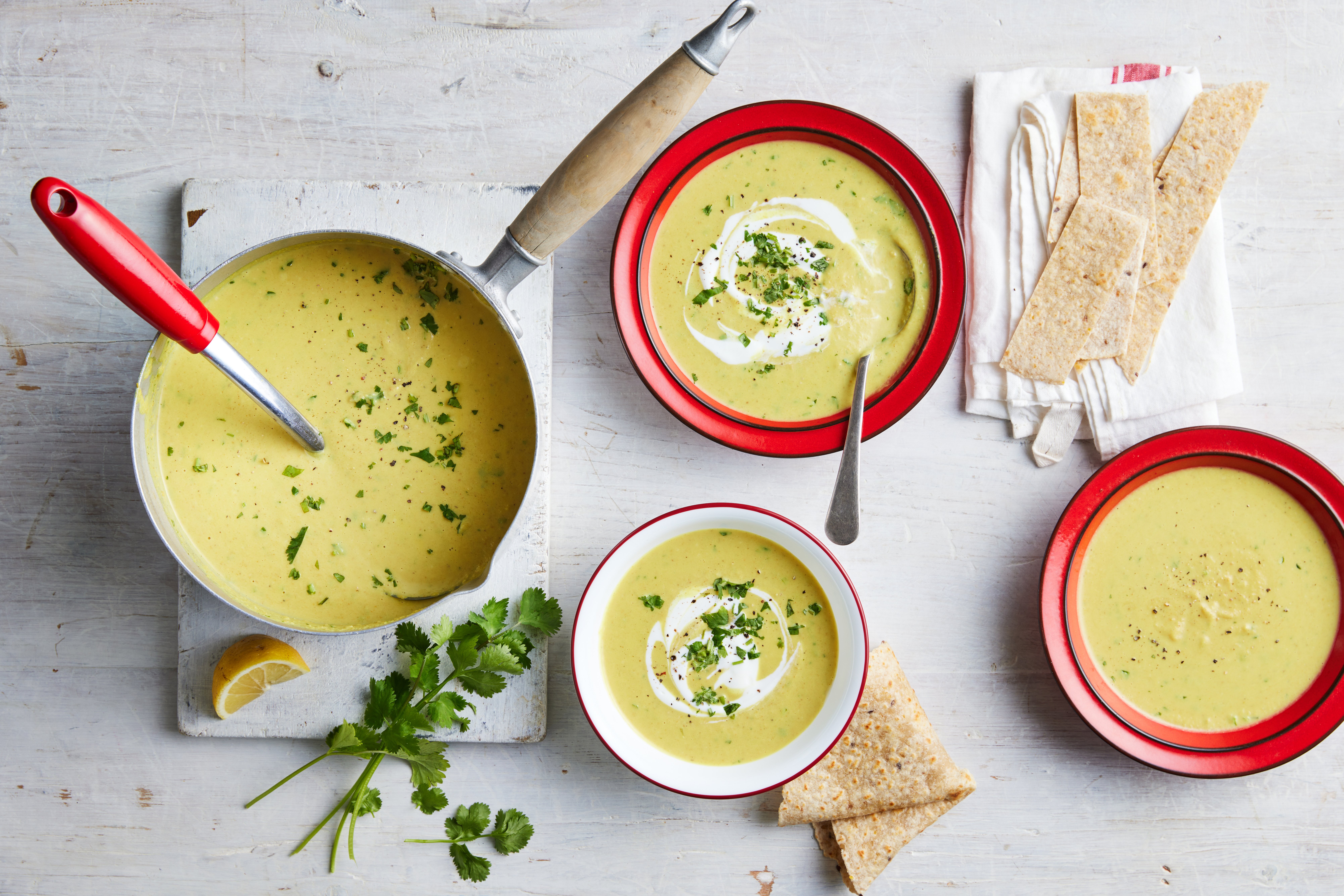 A bowl of soup, bread, and parsley on a table.