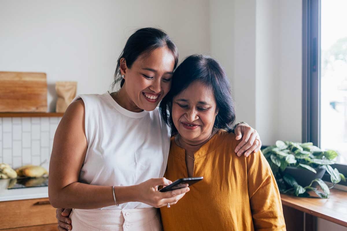 Mother and daughter smiling reading from a mobile arms over shoulder