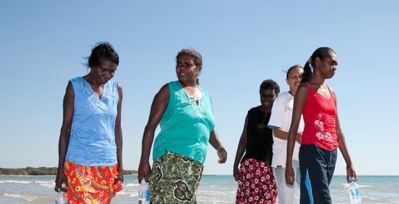 group of five First Nations women and girls walking on beach on a sunny day