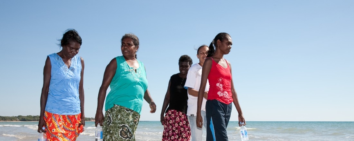 group of five First Nations women and girls walking on beach on a sunny day