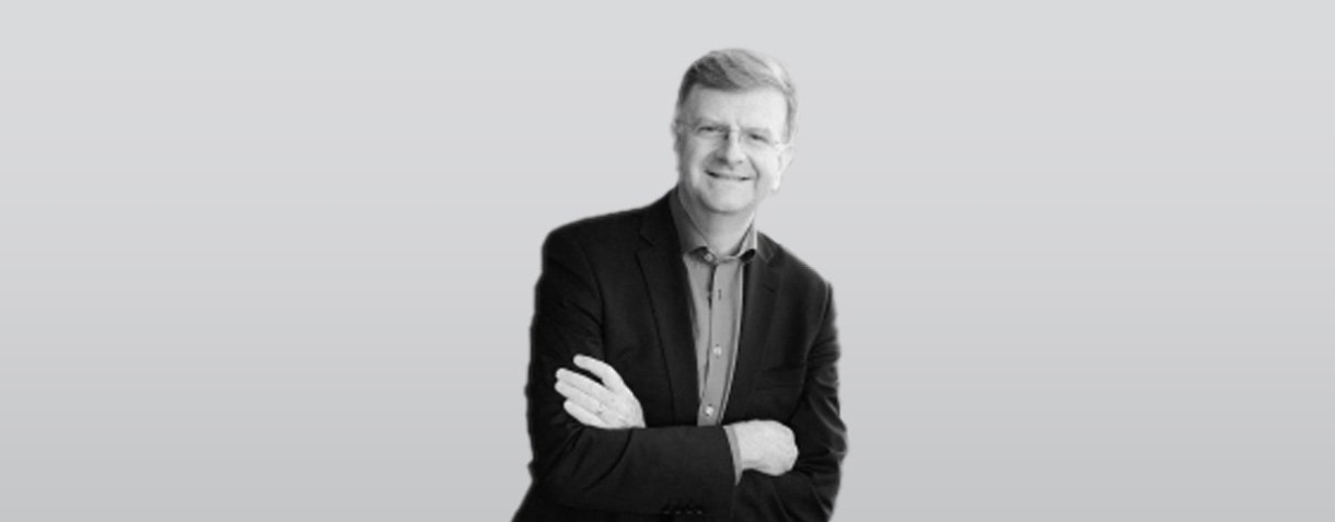 A professional man stands confidently with arms crossed, wearing a suit and tie.