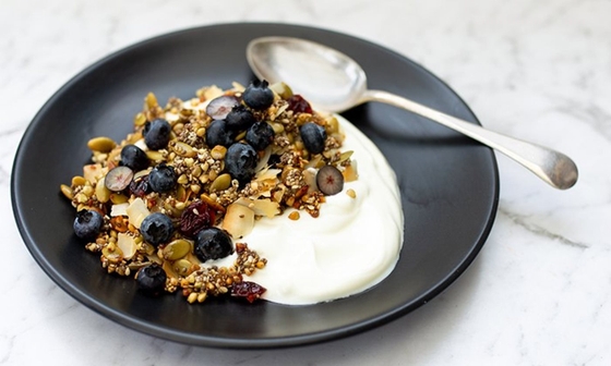 A bowl of granola topped with fresh blueberries and a variety of seeds