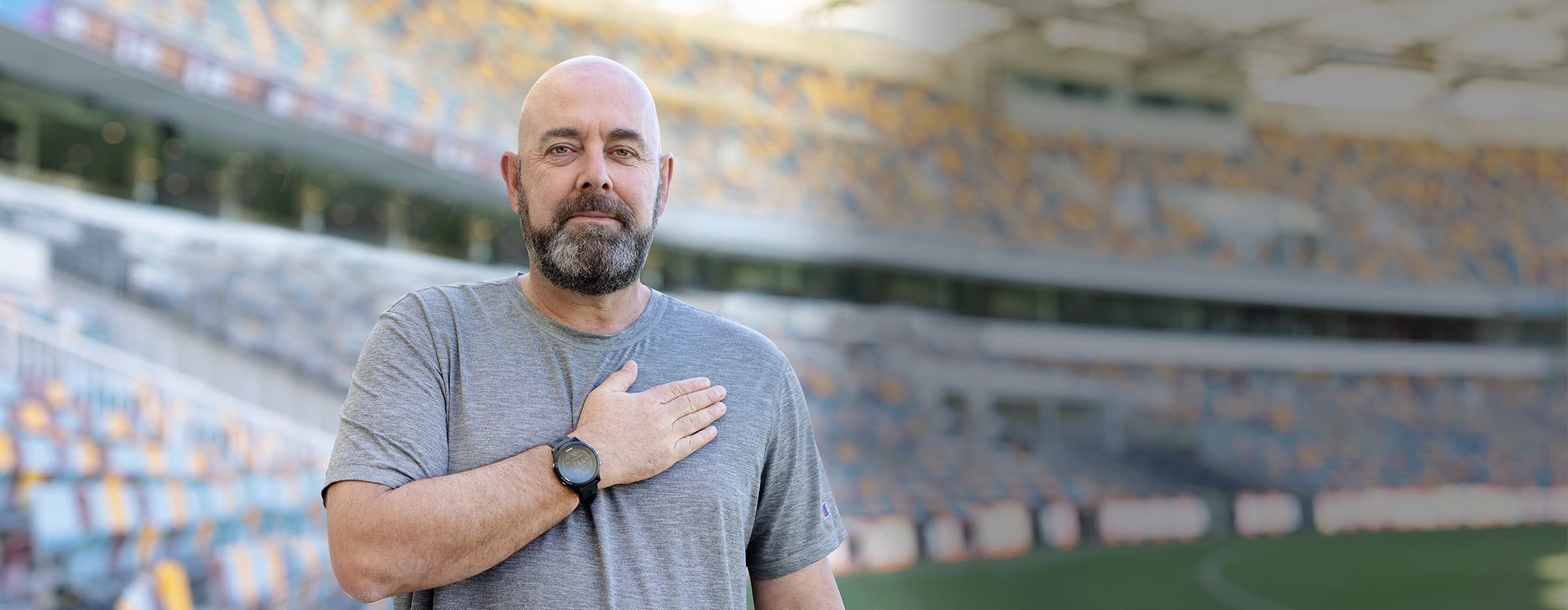 Darren Lehmann standing with a sporting stadium in the background, his hand on chest