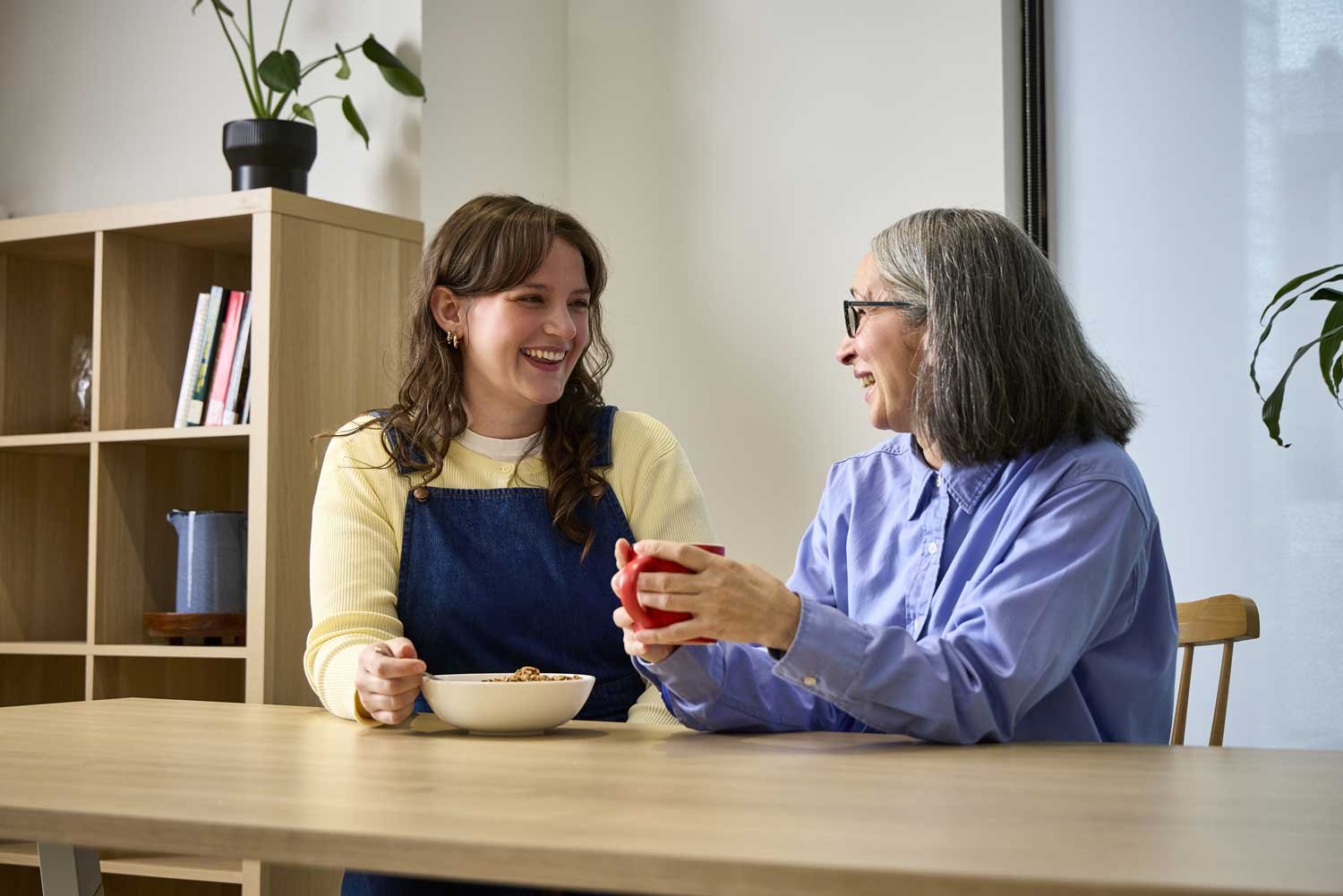 Two women laughing over a cuppa in an office kitchen setting