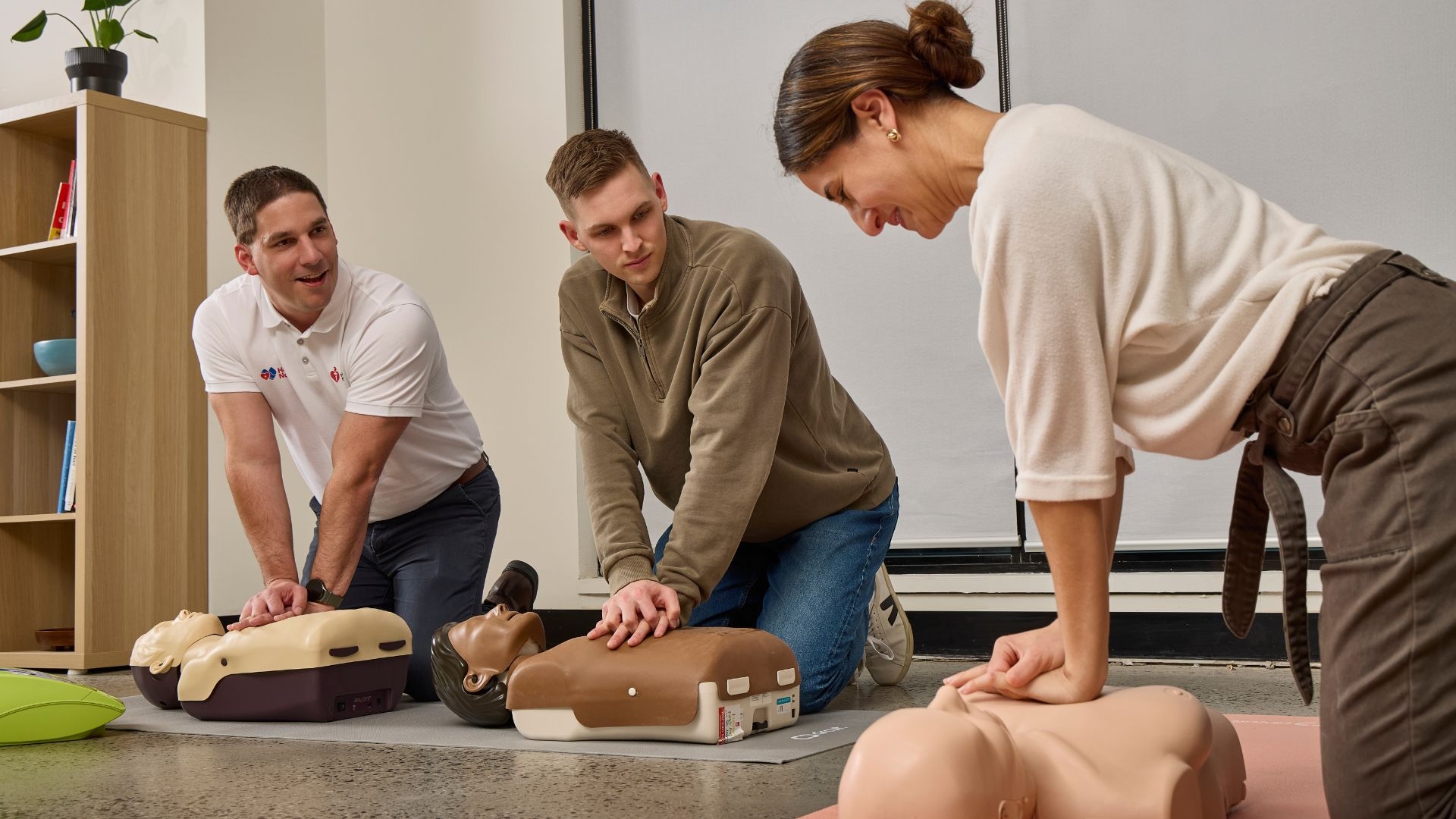 A couple of people learning how to do compressions on a mannequin