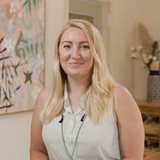 Carlye Weiner  in a white shirt admires a painting in front of her.