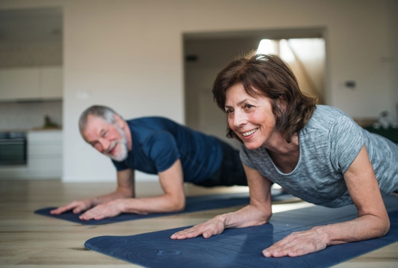 An older couple gracefully practicing yoga in their cozy living room, promoting health and relaxation.