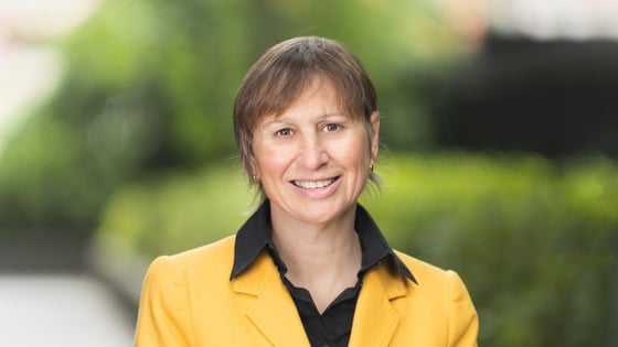 Professor Susan Davis smiling at the camera with a blurry background of green trees