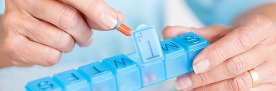 Person's hand holding pill organiser and other hand putting a pill in.
