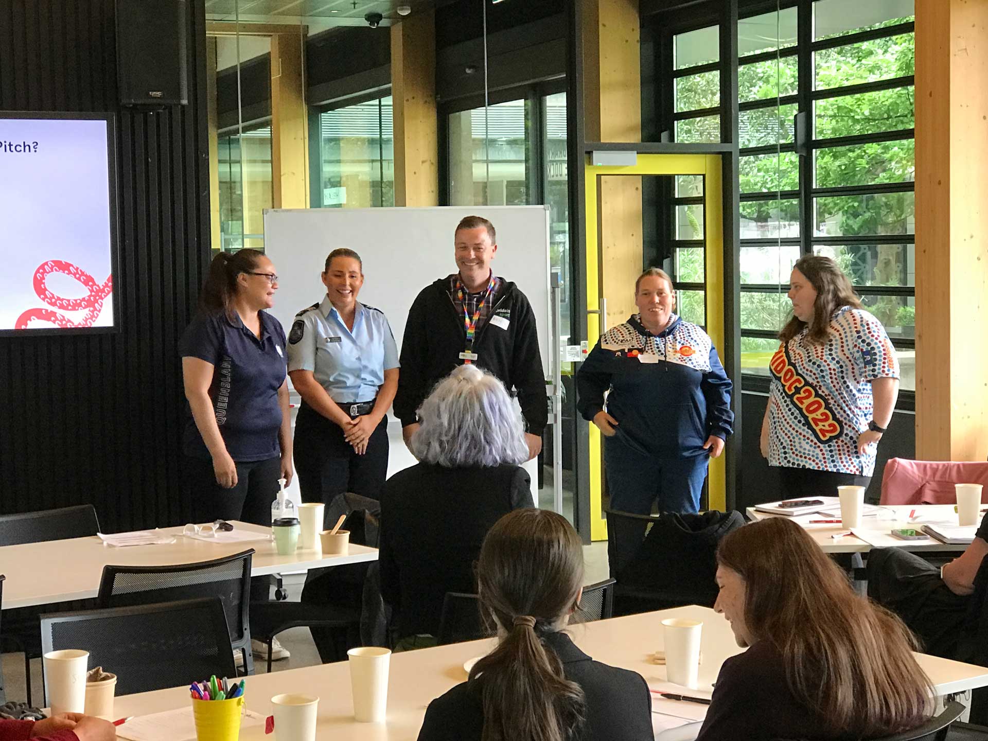 Group of five standing at the front of a room presenting