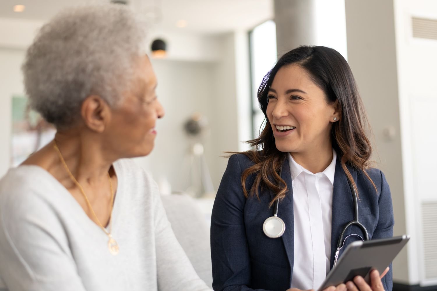 A healthcare professional speaking with an older person during a consultation, holding a tablet.
