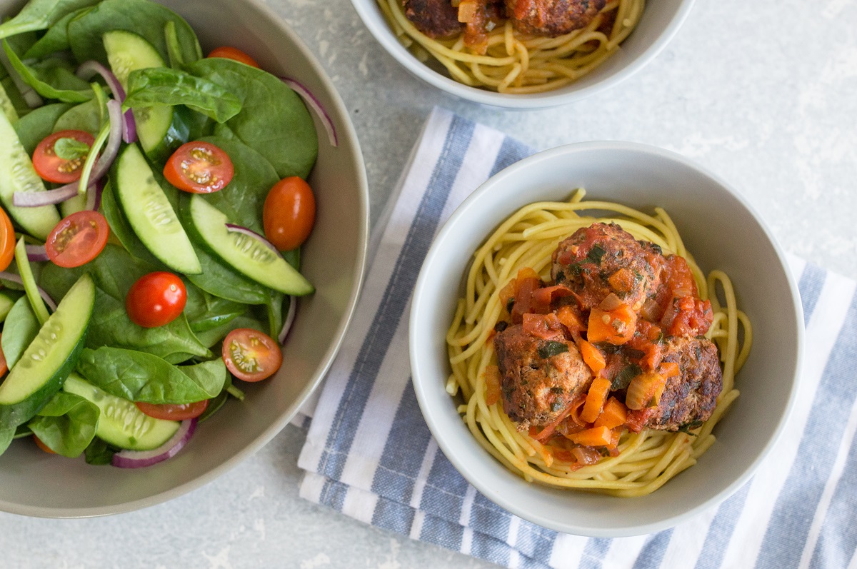 A delicious plate of spaghetti and meatballs topped with tomato sauce, served alongside a fresh salad
