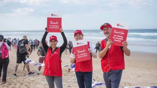 Heart Foundation team members on a beach holding up signs with words of encouragement to cheer on trekkers at an event.