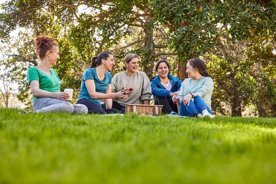 Group of five women sitting on park lawn