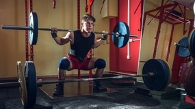 A focused young man squats with a barbell in a gym