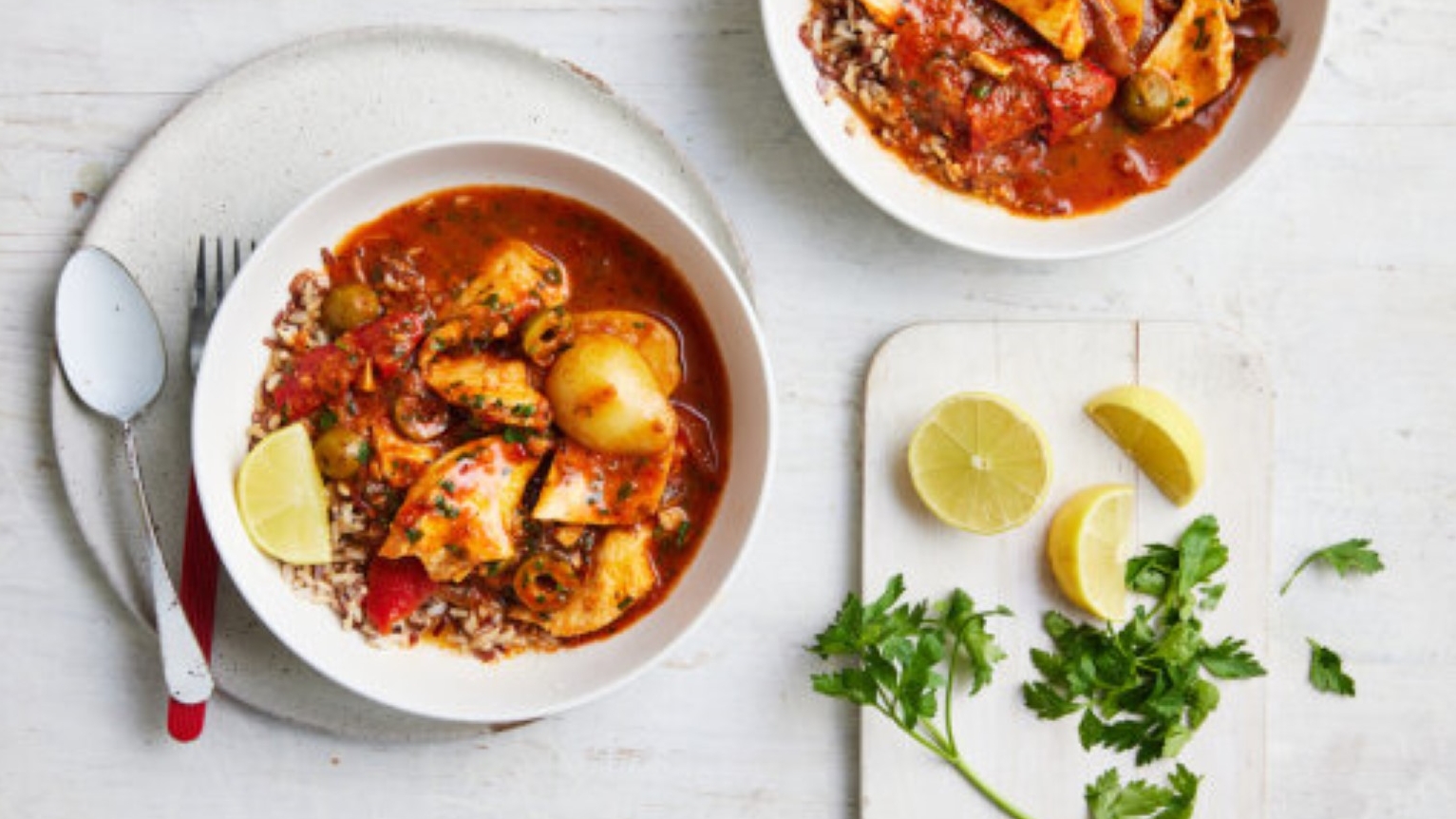 Spanish fish stew in bowls on a white table, with lemon wedges to serve